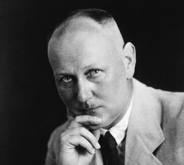 Gerhard Domagk stares towards the camera with his chin resting on his hand. he wears a light colored jacket with a dark tie.