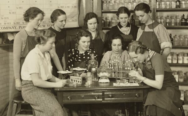 group of women standing around a lab table with periodic table in background